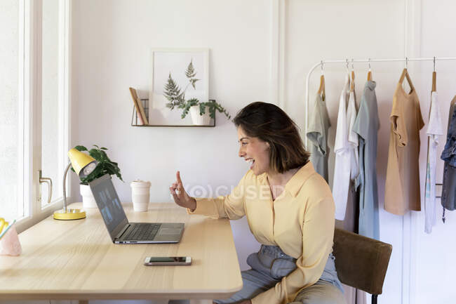 Cheerful young woman showing peace sign while enjoying video call to friends through laptop at home — Stock Photo