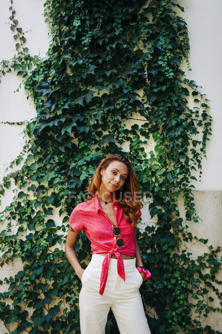 Woman with hands in pockets standing against wall covering with ivy at Aflama, Lisbon, Portugal — Stock Photo