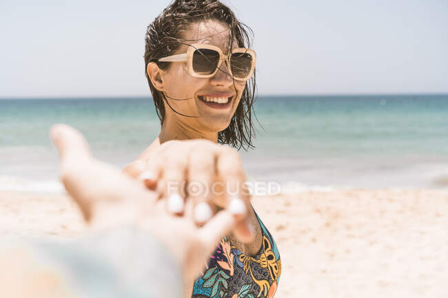 Donna sorridente con gli occhiali da sole che tiene per mano un amico maschio sulla spiaggia di Valdevaqueros, Tarifa, Spagna — Foto stock