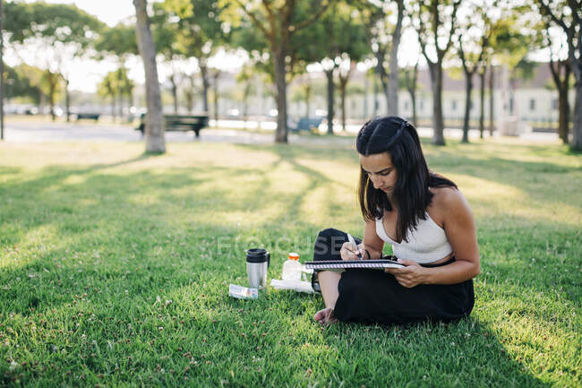 Young woman doing watercolor painting in book while sitting in park — Stock Photo