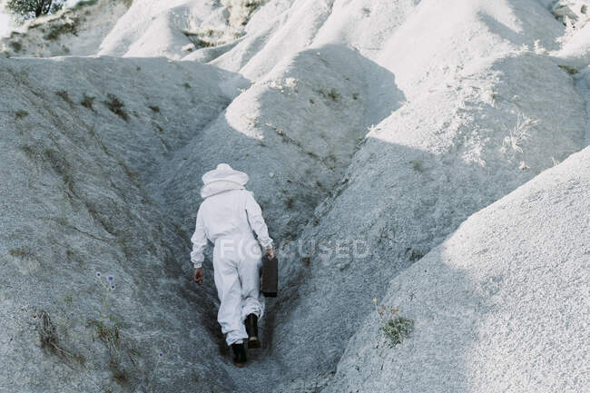 Homme avec mallette portant une robe d'apiculteur marchant dans un paysage apocalyptique sec — Photo de stock