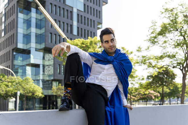 Бізнесмен в супергеройському мисі, що сидить на стіні в місті — стокове фото