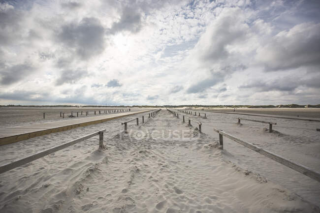 Clouds over wooden railings stretching along vast sandy beach — Stock Photo