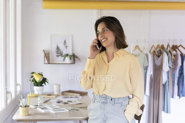 Joyeux propriétaire de magasin de vêtements parlant sur le téléphone intelligent tout en regardant loin — Photo de stock