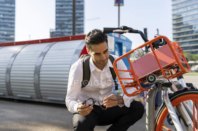 Pendolare maschio che ripara la bicicletta elettrica mentre si accovaccia in città — Foto stock