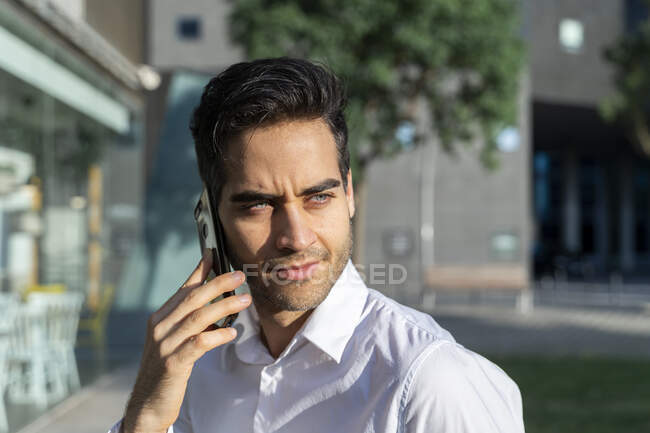 Gros plan d'un homme d'affaires confiant regardant ailleurs tout en parlant sur un téléphone intelligent — Photo de stock