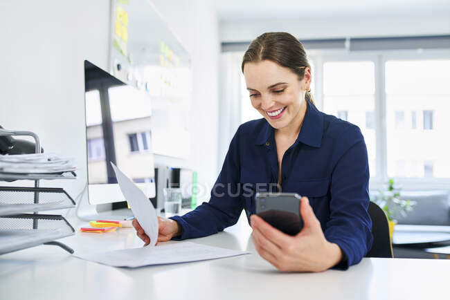 Sorridente donna d'affari creativa che legge documenti alla scrivania in ufficio — Foto stock
