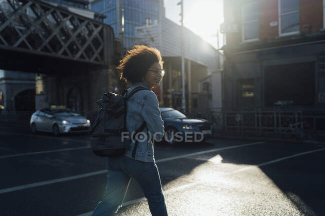 Afro jeune femme avec sac à dos traversant la rue en ville — Photo de stock
