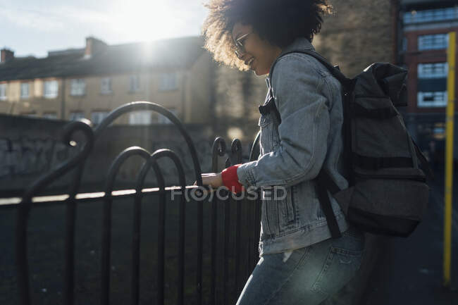 Unbekümmerte junge Frau mit Rucksack steht an sonnigem Tag am Geländer in der Stadt — Stockfoto