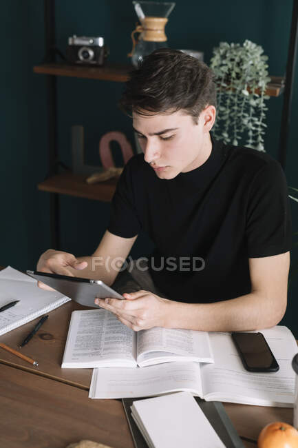 Наручний чоловік користується цифровою табличкою, сидячи за столом і роблячи домашнє завдання. — стокове фото