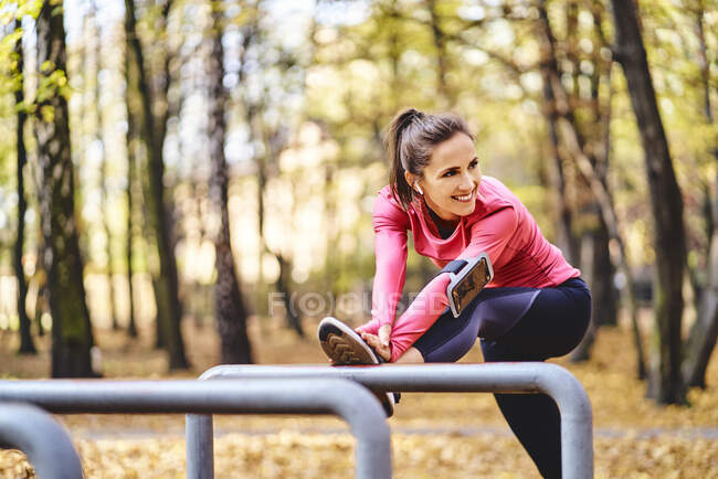 Young female jogger stretching her leg on bicycle stand in autumn forest — Stock Photo