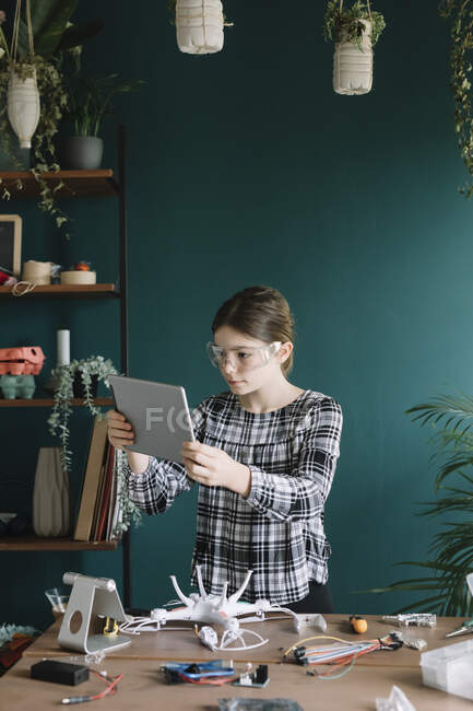 Chica usando tableta digital mientras que hace quadcopter en la mesa en casa - foto de stock