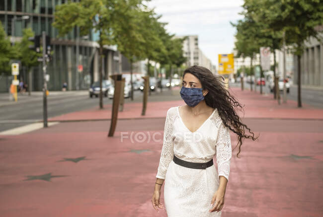 Jeune femme portant un masque regardant loin tout en marchant sur le sentier en ville — Photo de stock