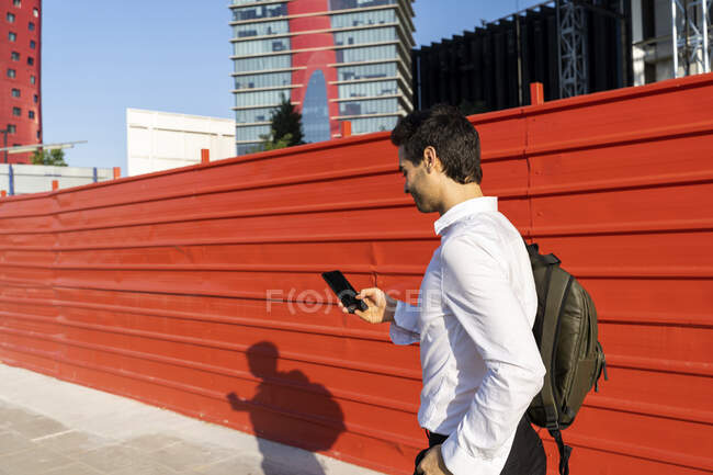 Homme entrepreneur utilisant un téléphone portable tout en marchant par mur dans la ville — Photo de stock