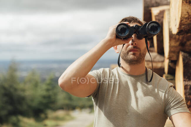 Caminhante masculino olhando através de binóculos enquanto está de pé contra o céu na floresta — Fotografia de Stock