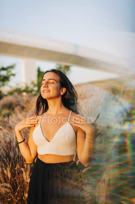 Молодая женщина с закрытыми глазами стоит на фоне сухой травы на открытом воздухе — стоковое фото