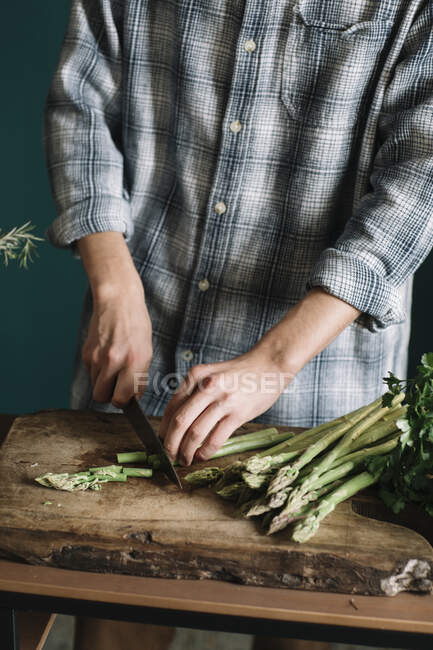 Parte central do homem cortando espargos frescos a bordo na cozinha — Fotografia de Stock