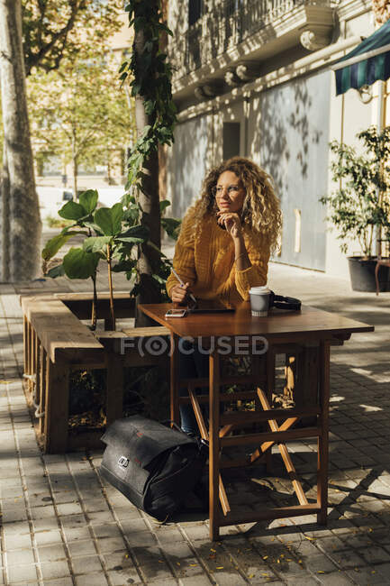 Думаюча молода жінка відвернулася, сидячи в кафе на тротуарі в місті. — стокове фото