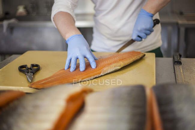 Hombre cortando pescado en el mostrador en planta de procesamiento de alimentos - foto de stock