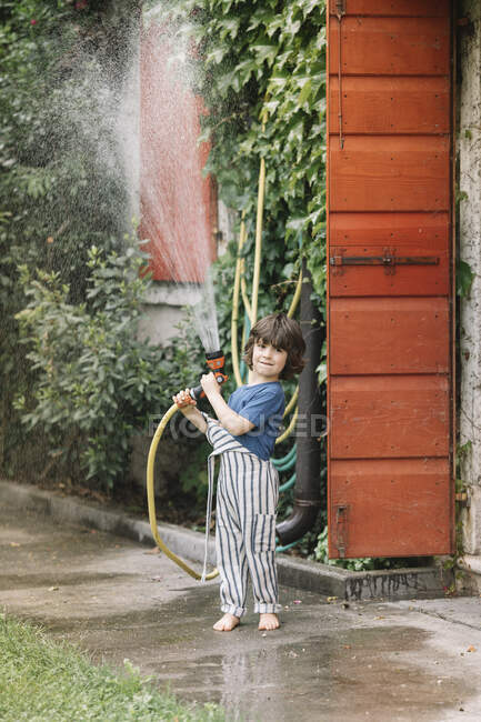 Ragazzo che gioca con tubo da giardino mentre in piedi in cortile — Foto stock