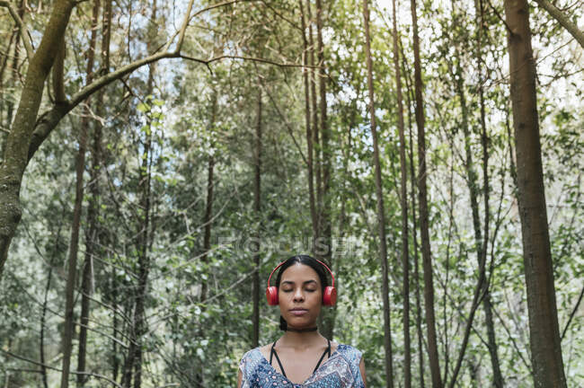 Giovane donna con gli occhi chiusi ascoltare musica attraverso le cuffie contro gli alberi al parco — Foto stock