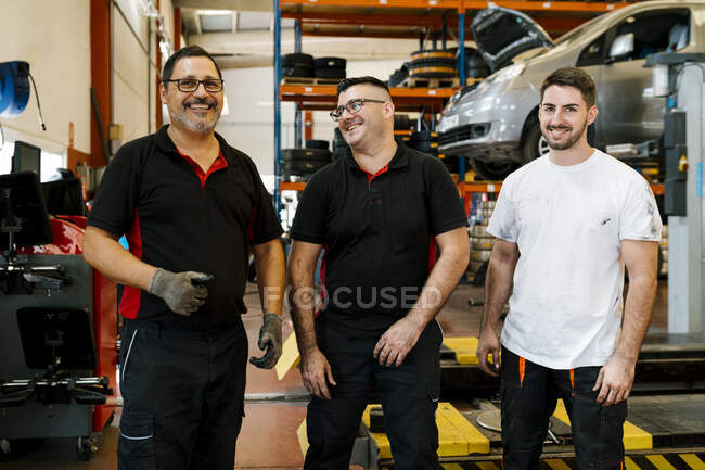 Lächelnde männliche Kollegen stehen in der Autowerkstatt — Stockfoto