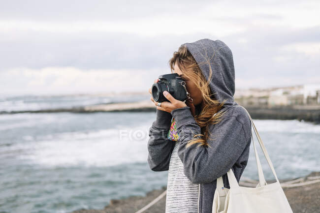 Жінка фотографує з фотоапаратом стоячи на пляжі. — стокове фото