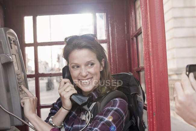 Smiling woman holding telephone receiver while looking at friend photographing through smart phone — Stock Photo
