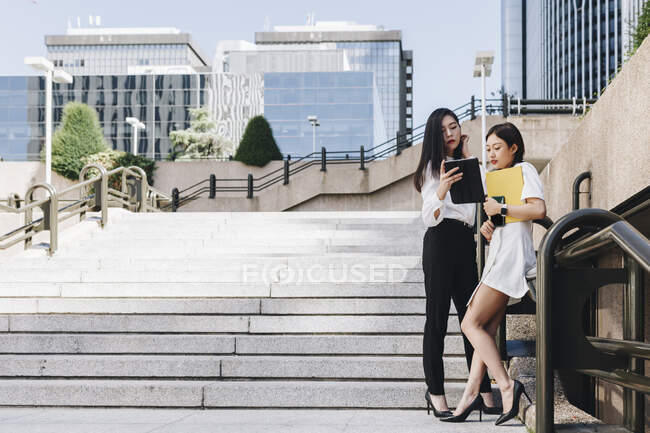 Imprenditrici in piedi sulle scale contro il quartiere del centro, mentre utilizzando tablet digitale — Foto stock