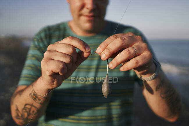 Primer plano del hombre adulto medio preparando el camino de pesca en la playa durante el atardecer - foto de stock