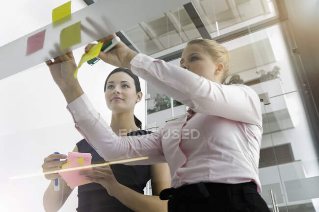 Colleghi di sesso femminile attaccare note adesive sulla parete di vetro in ufficio — Foto stock
