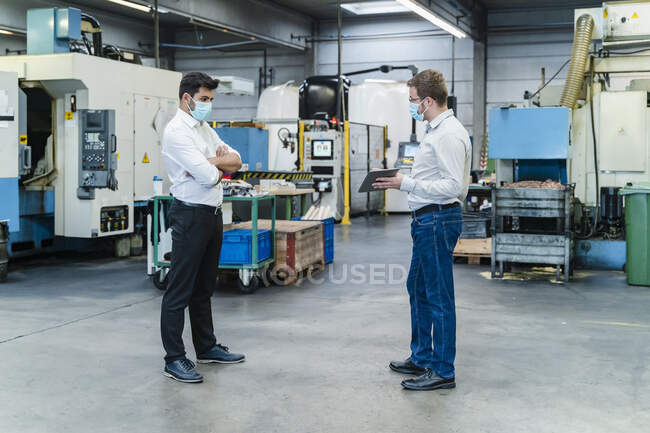 Male coworkers discussing while maintaining social distancing in factory — Stock Photo