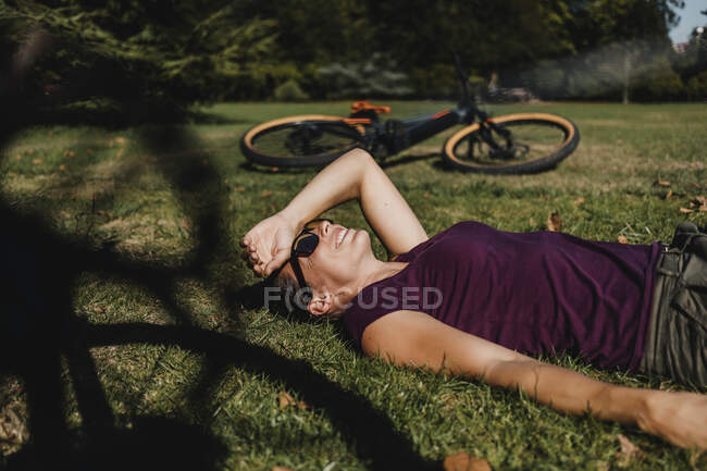 Mulher deitada na grama enquanto descansa de bicicleta de montanha no parque — Fotografia de Stock