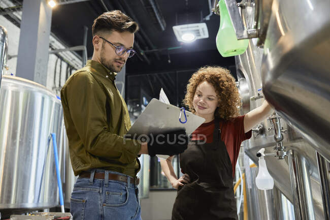 Hombre y mujer que trabajan en el documento de verificación de la cervecería artesanal - foto de stock
