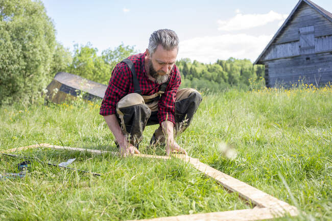 Carpenter crouching while positioning planks on grass — Stock Photo