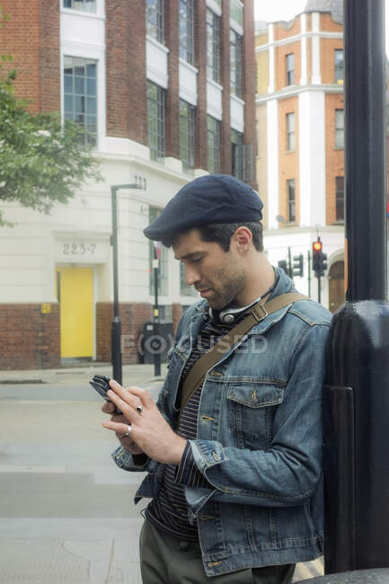 Взрослый мужчина с помощью мобильного телефона, опираясь на столб в городе — стоковое фото