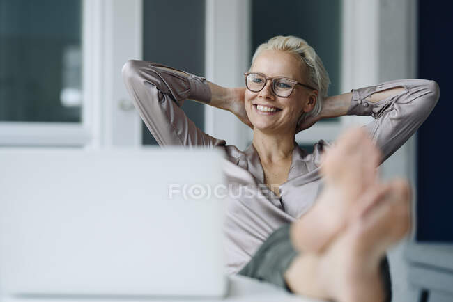 Ragionevole donna d'affari con le mani dietro la testa rilassante alla scrivania in ufficio — Foto stock