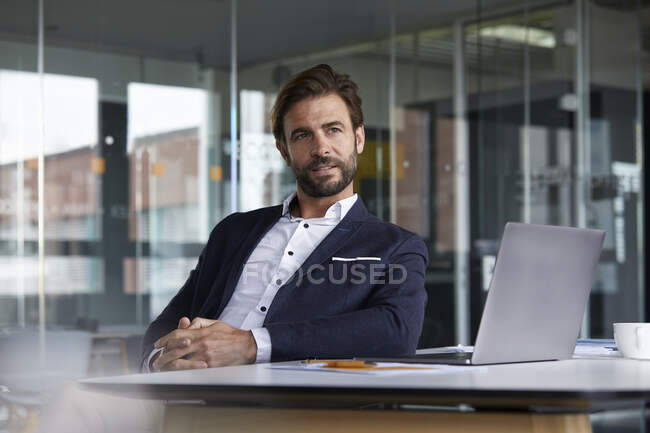 Thoughtful businessman with laptop sitting on chair in office — Stock Photo