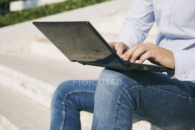 Человек печатает на ноутбуке, сидя на улице в солнечный день — стоковое фото