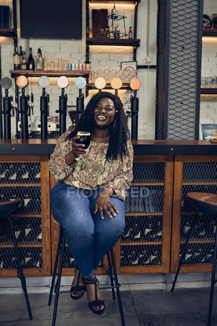 Щаслива жінка сидить за прилавком у пабі з пивом — стокове фото