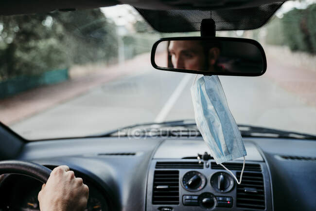 Close-up of protective face mask hanging on rear-view mirror in car — Stock Photo