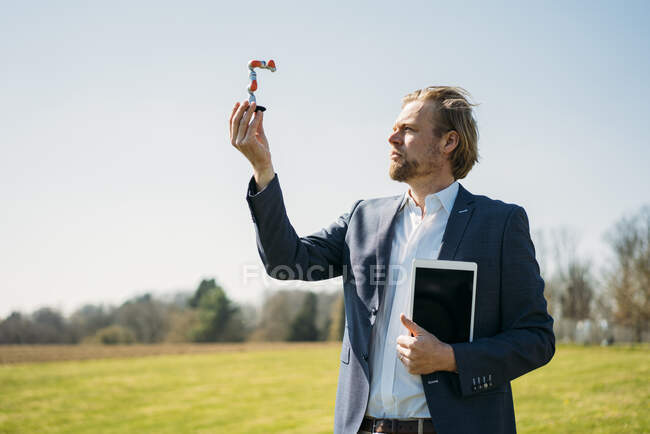 Empresário analisando em pequeno braço robótico enquanto segurava tablet digital contra céu limpo durante o dia ensolarado — Fotografia de Stock