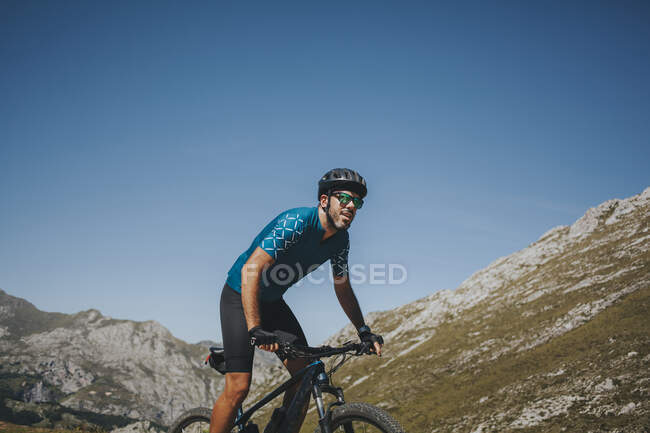 Male cyclist riding mountain bike against sky on sunny day, Picos de Europa National Park, Asturias, Spain — Stock Photo
