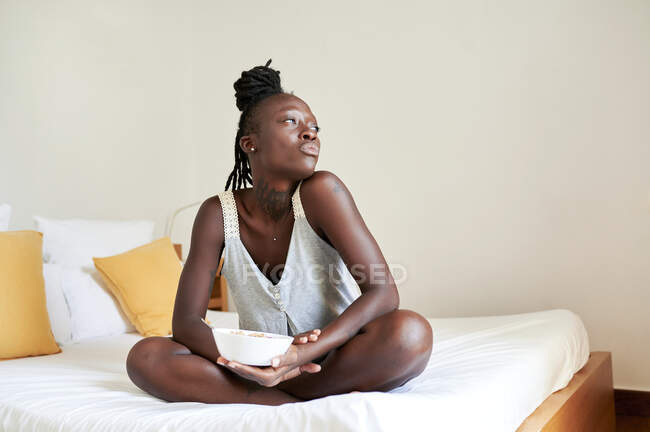 Думаюча молода жінка з перекусами сидять на ліжку. — стокове фото