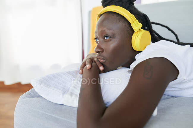 Primo piano di una giovane donna premurosa che ascolta musica mentre è sdraiata sul divano di casa — Foto stock