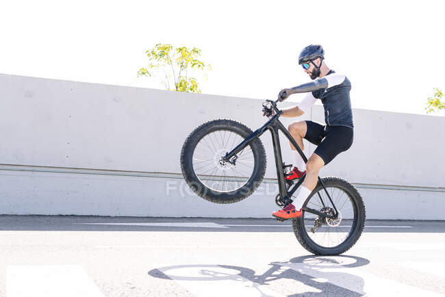 Athlète masculin avec un membre artificiel effectuant cascade avec vélo sur la route contre ciel clair — Photo de stock