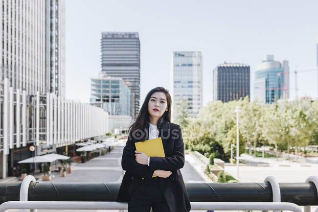 Confident businesswoman with book standing against downtown district in city — Stock Photo