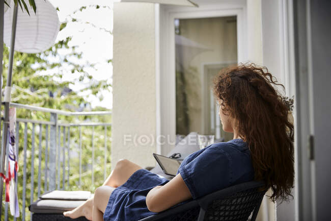 Femme lisant à partir e-reader assis sur une chaise sur le balcon — Photo de stock