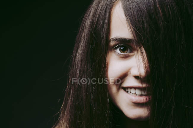 Primer plano de la chica sonriente con el pelo castaño en la cara contra el fondo negro - foto de stock