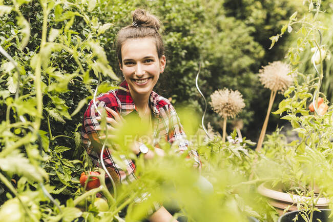 Smiling beautiful woman sitting amidst plants in vegetable garden - foto de stock